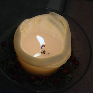 Bild einer brennenden weißen Kerze, vor dunklem Hintergrund